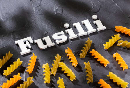Fusilli phrase in wooden letters - Spiral raw pasta of different colors