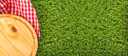 Chopping board and red checkered napkin on the green grass.の写真素材