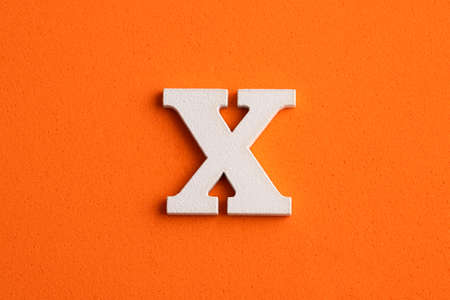Alphabet letter X - White wood piece on orange foamy background