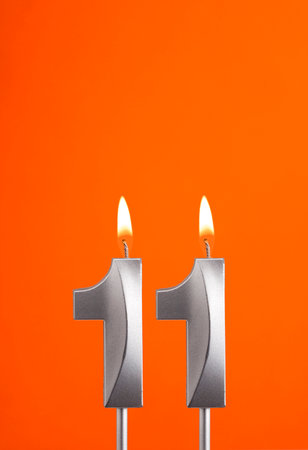 Number 11 - Burning anniversary candle on orange foamy backgroundの写真素材
