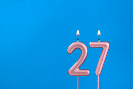Number 27 - Burning anniversary candle on blue foamy backgroundの写真素材