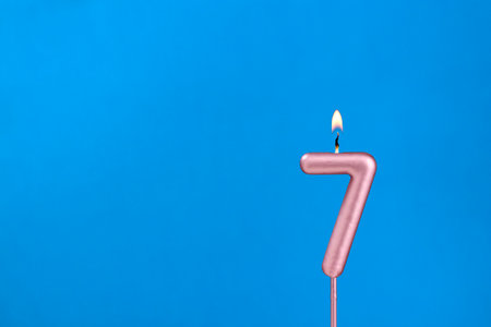Number 7 - Burning anniversary candle on blue foamy background