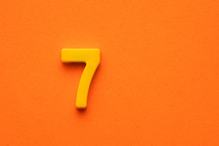 Yellow number 7 - plastic piece on orange foamy backgroundの写真素材