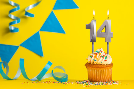 Lighted birthday candle number 14 - Yellow background with blue pennantsの写真素材