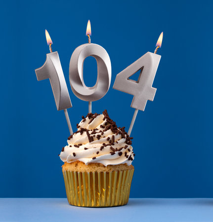 Vertical birthday card with cake - Lit candle number 104 on blue backgroundの写真素材