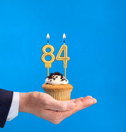 Hand holding a cupcake with the number 84 candle - Birthday on blue backgroundの写真素材