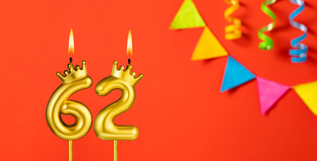 Number 62 candle - Birthday celebration on an orange background with pennantsの写真素材