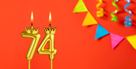 Number 74 candle - Birthday celebration on an orange background with pennants