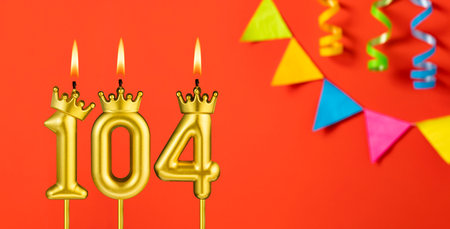 Number 104 candle - Birthday celebration on an orange background with pennantsの写真素材