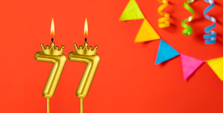 Number 77 birthday candle on an orange background with pennantsの写真素材