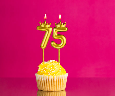 Yellow birthday cupcake with a number 75 candle - Birthday card on a pink backgroundの写真素材