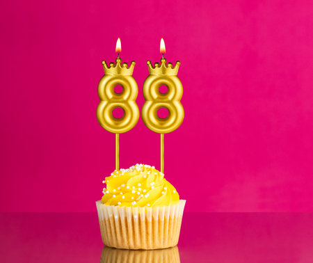 Birthday celebration with number 88 candle - Yellow cupcake on a pink backgroundの写真素材