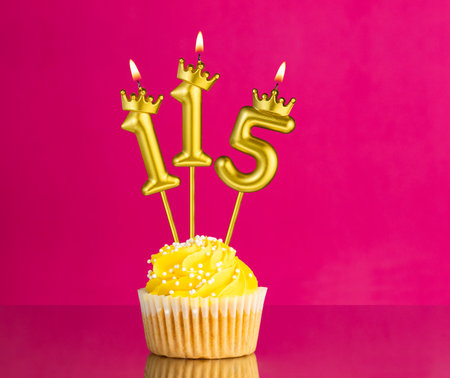 Yellow birthday cupcake with a number 115 candle - Birthday card on a pink backgroundの写真素材