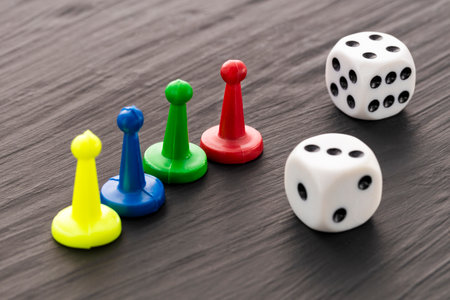 Colored game tokens and two white dice with black dots on a dark backgroundの写真素材
