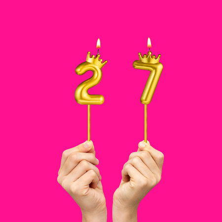 Birthday on a fuchsia background with the number 27 - Hands holding number-shaped candlesの写真素材