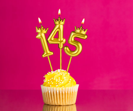 Yellow birthday cupcake with a number 145 candle - Birthday card on a pink background