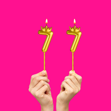 Birthday on a fuchsia background with the number 77 - Hands holding number-shaped candlesの写真素材