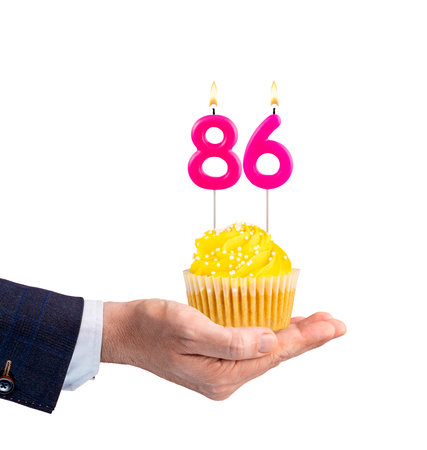 Hand holding a birthday cupcake - Pink candle, number 86 on a white backgroundの写真素材