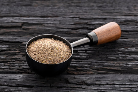 Ground black pepper in a measuring spoon on a wooden background - Piper nigrum