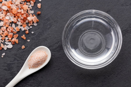 Himalayan pink salt next to a clear container of water on a dark slate surfaceの写真素材
