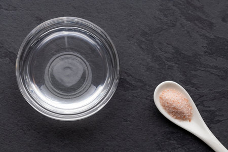 Himalayan salt next to a bowl of water on a dark background, a concept of purity and natural...