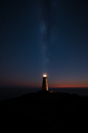 A lighthouse glowing by the sea at nightの素材