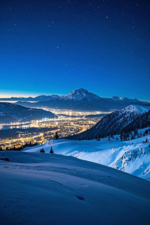 A city brightly lit at night under the snow capped mountainsの素材