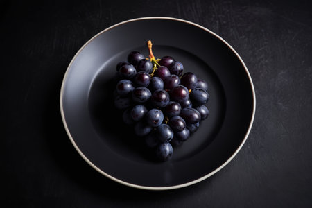 Fresh purple grapes on a black plateの素材