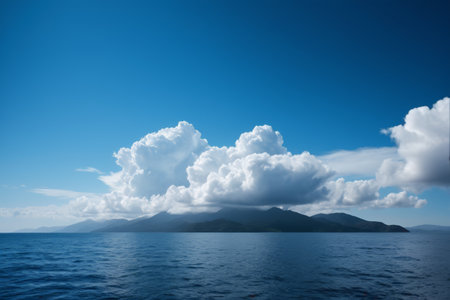 The vast ocean and distant mountains under the blue sky and white cloudsの素材