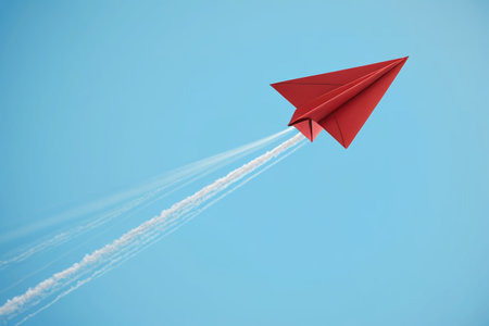 Red paper plane flying in blue skyの素材