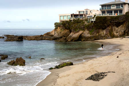 Laguna Beach, California / USA - March 10, 2019: Young woman walks alone in early morning on deserted beach, surrounded by cliffs and luxury homes at Wood's Cove in Laguna Beach, a travel destination.のeditorial素材