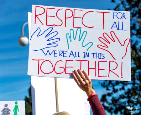 Close-up of a hand-drawn sign proclaiming, "Respect for All. We're All in this Together!" Group of demonstrators on the street with a signboard at a rally.の写真素材