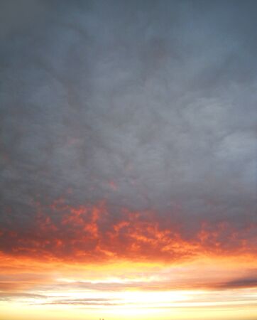 Cloudy sunset 8, a dramatic sunset with firey golds, oranges and reds on the botton of a cloud layer の写真素材