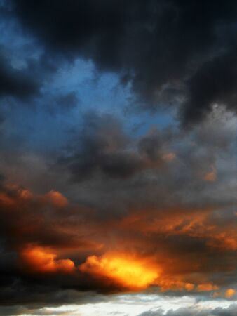 a dramatic sunset with firey golds, and oranges on the botton of a cloud layer.の写真素材