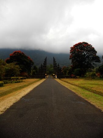Balinese entrance with large tropical trees and a cloud-covered moutainの写真素材