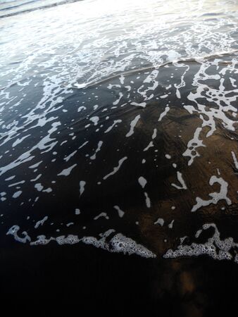 ocean foam over black sand