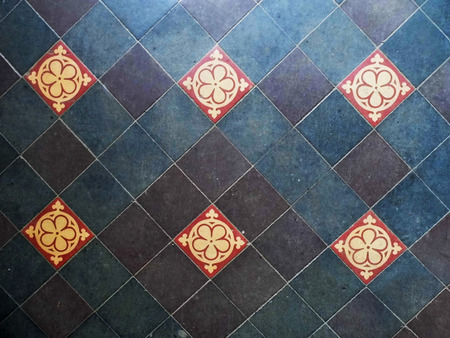 Old tiled floor in old British building, with plain hand-made blue and purple tiles, and patterned red and yellow tiles every 3 tiles.の写真素材