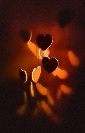 Hanging heart shapes, top-down angled view a group of small hearts hanging at different heights on rough threads, with shadows, vignette blur, orange tints.の写真素材