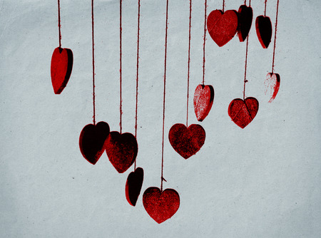 Glitter hearts, a group of hearts covered with silver glitter, hanging from threads, red tints, gray paper texture background.の写真素材