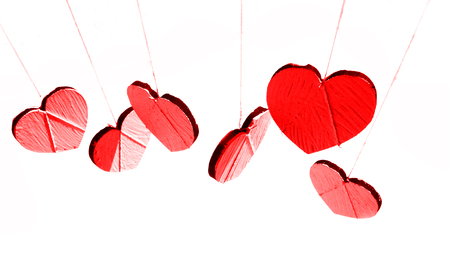 Hanging heart shapes, a row of small pale hearts hanging on rough threads, white background, red tints.の写真素材
