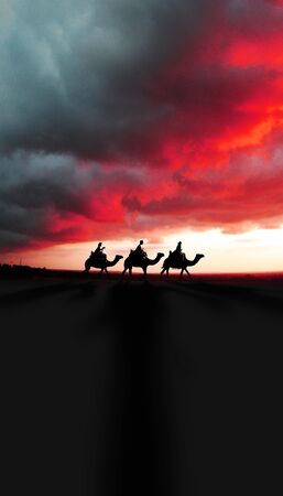 Three Kings Christmas card with the 3 wise men on camels on a simple desert landscape with shadows 3D image, with a dramatic red real sunset, tall.の写真素材