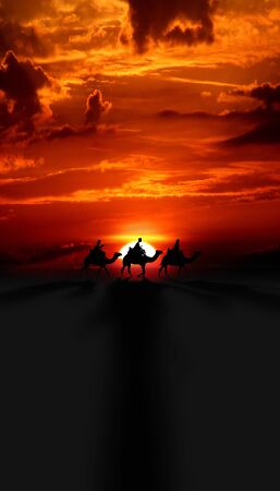 Three Kings Christmas card with the 3 wise men on camels on a simple desert landscape with shadows 3D image, with a real orange and red sunset, tall.の写真素材