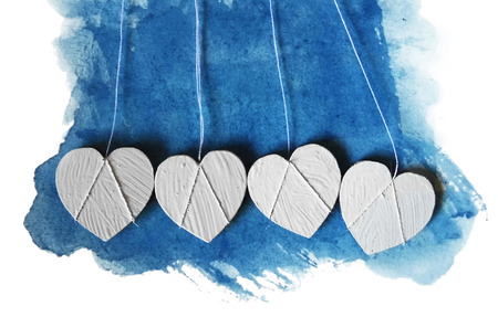 Four real wooden white-painted heart-shapes on a blue watercolor painted background.の写真素材