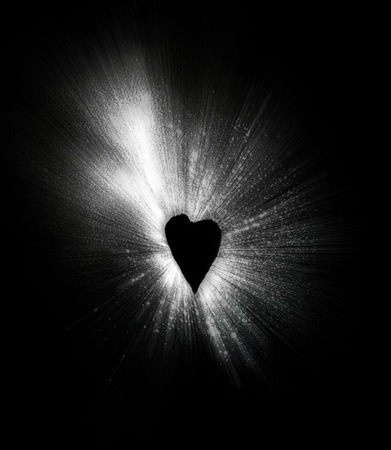 Heart-shaped negative space left by talcum powder thrown onto black paper, zoom blurred.の写真素材