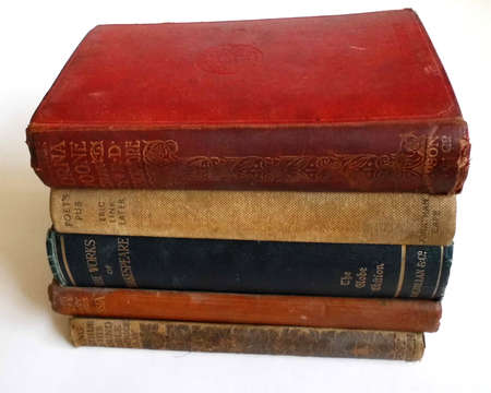 Old books in a row on a white surface, side lit, with shadow.の写真素材