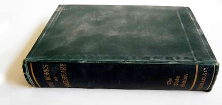 Old book with a dark cover lying on a surface, lit from the side with shadow.の写真素材