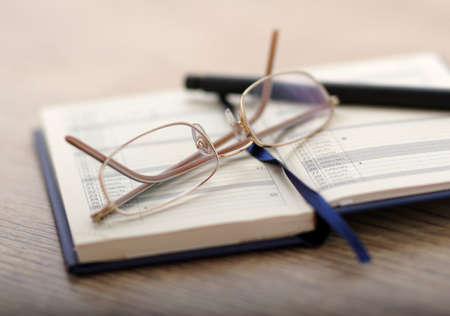 Note-book, glasses and a pen on a wooden tableの写真素材