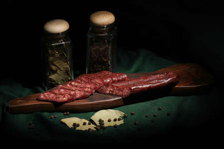 Still life composition with sliced flat sausage on a platter and spices.の写真素材