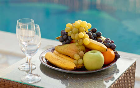 Fresh fruits and glasses near blue waterの写真素材