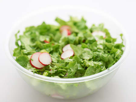 Green lettuce and red radish salad in transparent plastic cup on whiteの写真素材